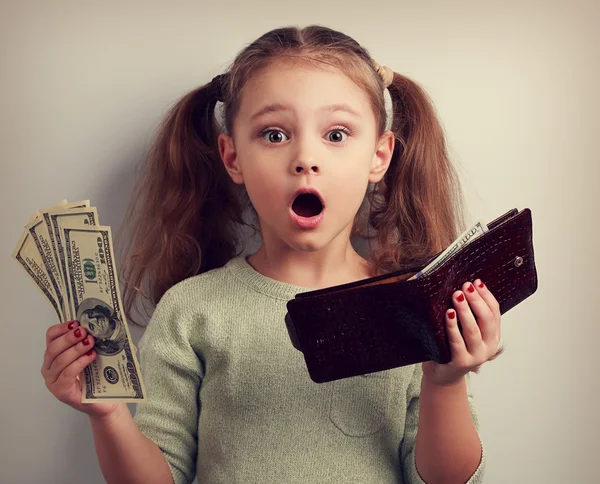Cute surprising kid girl holding wallet and dollars with open mo