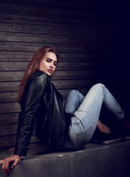 Sexy young woman in black leather jacket sitting on the stone an