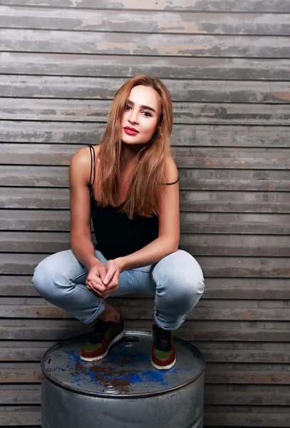 Happy beautiful woman in blue jeans sitting on the iron barrel o