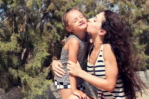 Happy mother kissing her fun enjoying daughter on summer geen ba