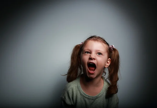 Angry child girl screaming with opened mouth and looking up with evil