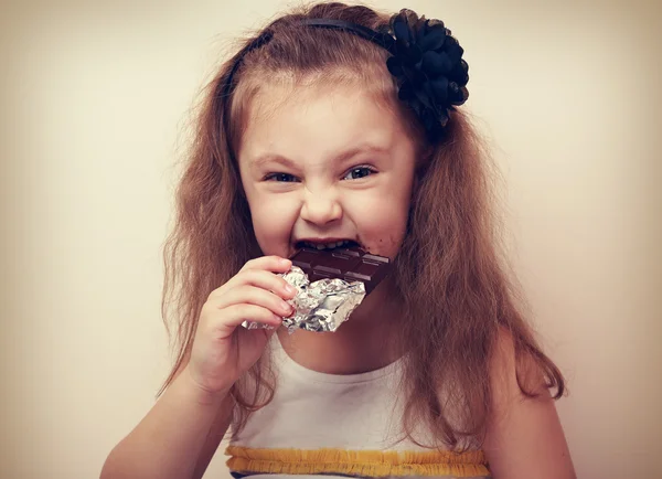 Happy fun smiling kid girl biting dark chocolate with craving ey