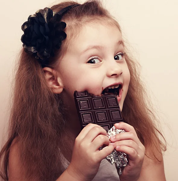 Happy cute beautiful kid girl biting sweet chocolate. Vintage po