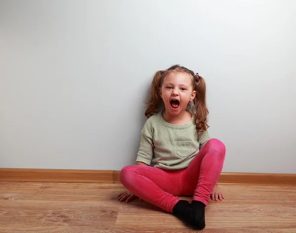 Happy crying kid with open mouth sitting on the floor
