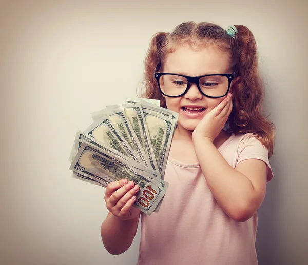 Surprising emotional kid girl holding dollars in hand and thinki