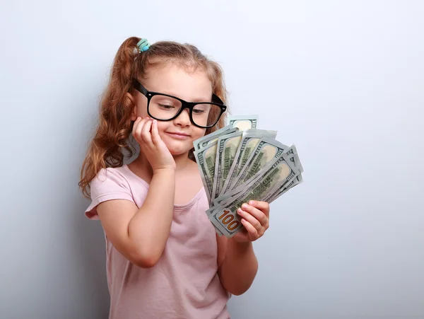 Dreaming cute kid girl looking on money and thinking how can spe