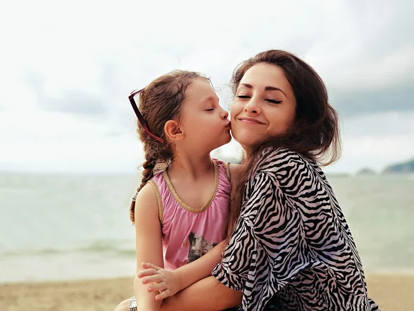 Cute kid girl kissing her happy enjoying mother with closed eyes