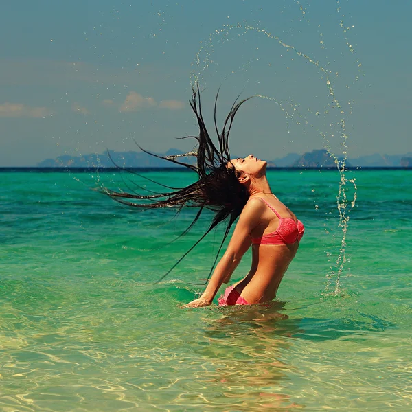 Beautiful model woman splashing her hair in turquoise azure wate