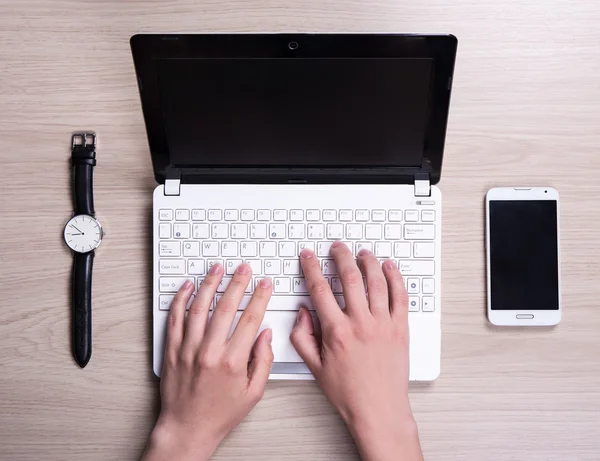 Hands with white laptop, smart phone and watch on the table