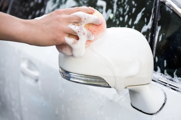 Male hand washing car mirror with sponge