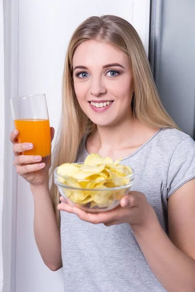 Portrait of happy young woman eating chips and drinking juice