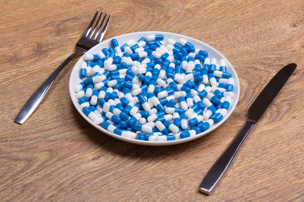Blue pills in plate with knife and fork on wooden table