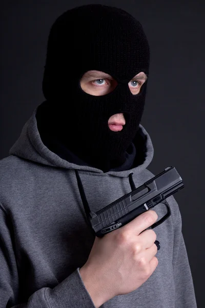 Man criminal in black mask with gun over grey