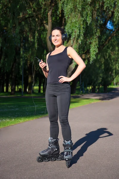 Happy young brunette woman on roller skates listening music in p