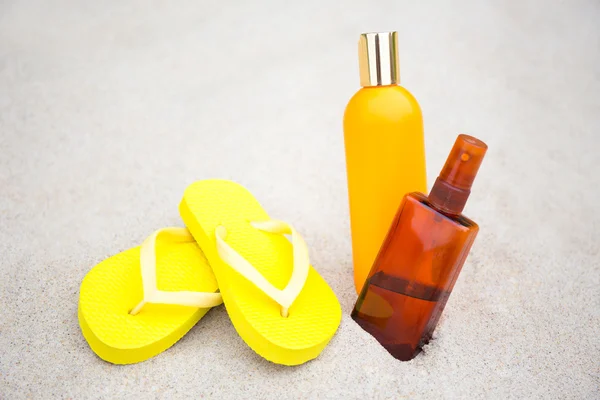 Skin care concept - flip flops and suntan lotion bottles in sand
