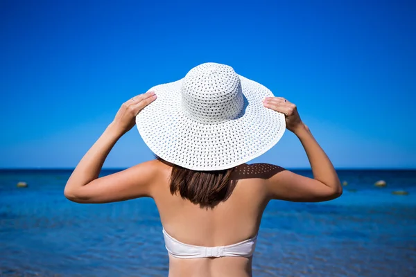 Back view of slim woman in bikini and hat looking at the sea