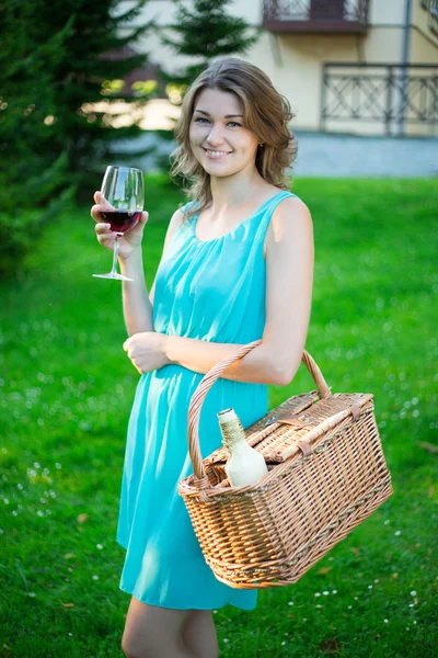 Happy beautiful woman with picnic basket and glass of wine in pa