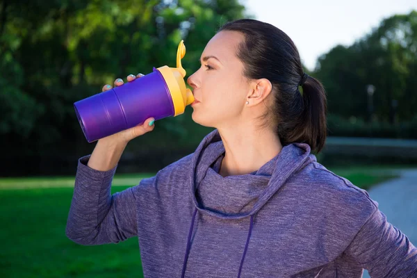 Close up of fitness woman drinking water from bottle in park