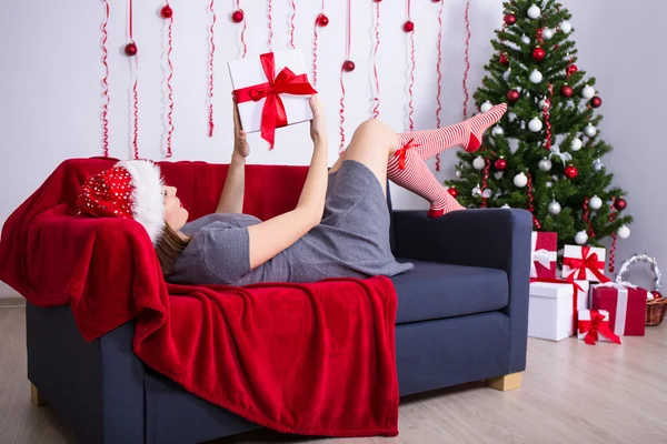 Young woman lying on sofa with decorated Christmas tree at home