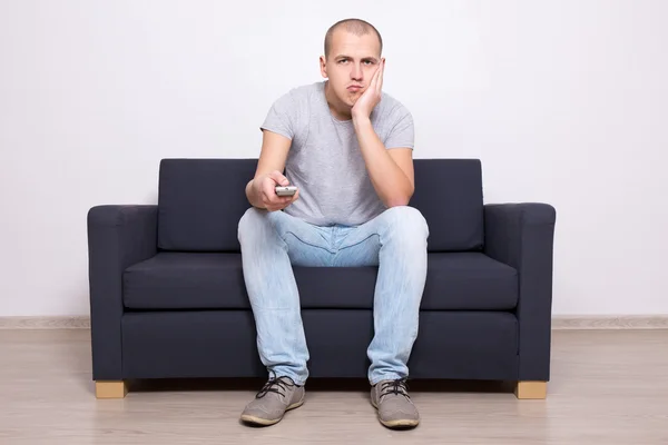 Bored man sitting on sofa and watching tv