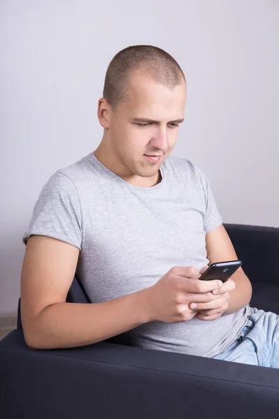 Portrait of handsome man sitting on sofa and using smart phone