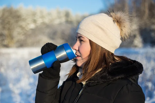 Frost concept - beautiful woman with thermal mug in winter fores