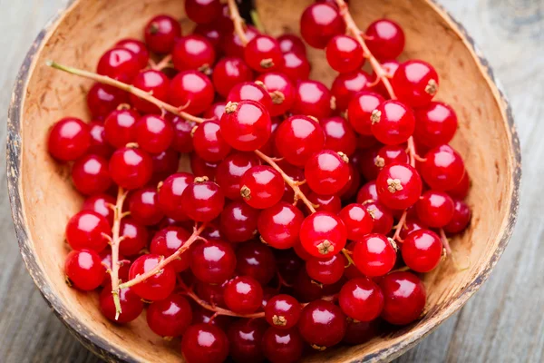 Redcurrant on a branch close to a wooden bowl.