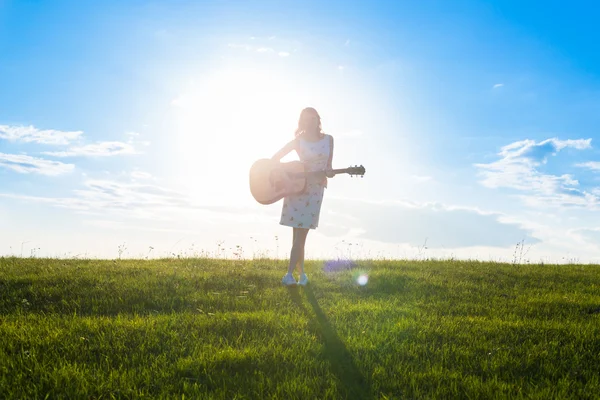 Woman in dress holding the guitar on cloudy sunset sky