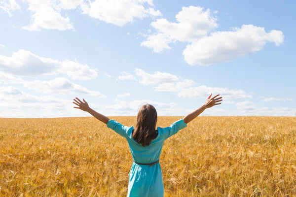 Young woman enjoying sunlight with raised arms in straw field