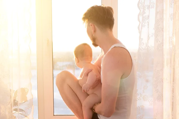 Portrait of father standing near the window with baby
