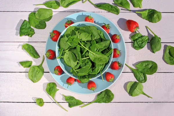 Fresh spinach salad with spinach and strawberries on wooden light pink table