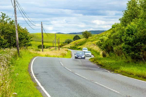 Winding road in the hills of Scotland with cars, sunny sumer day