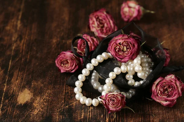 Vintage pearl with dry pink roses on a wooden background