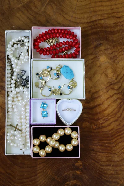 Necklaces, rings, earrings, pearls and gold in boxes on a wooden background