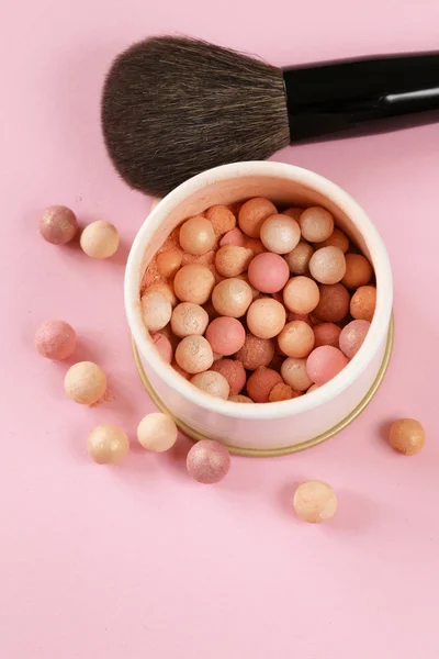 Cosmetics rouge balls in the bank on a pink background