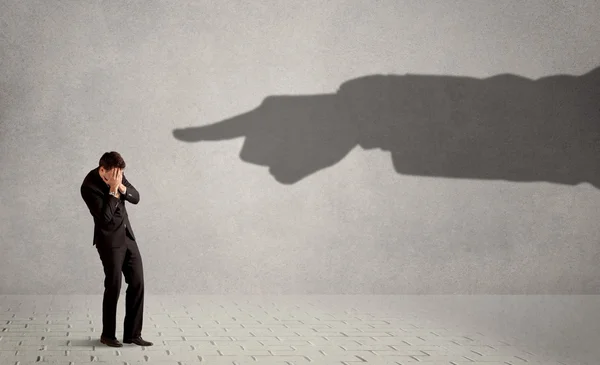 Business person looking at huge shadow hand pointing at him conc