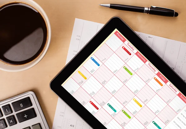 Tablet pc showing calendar on screen with a cup of coffee on a d