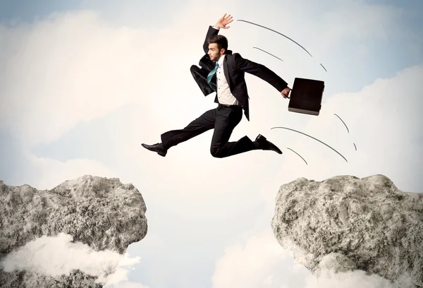 Happy business man jumping over a cliff
