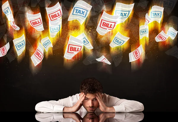 Depressed businessman sitting under burning tax and bill papers