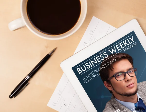 Tablet pc showing magazine on screen with a cup of coffee on a d