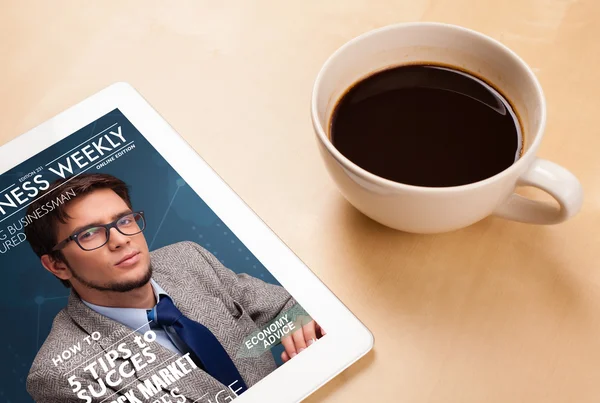 Tablet pc showing magazine on screen with a cup of coffee on a d