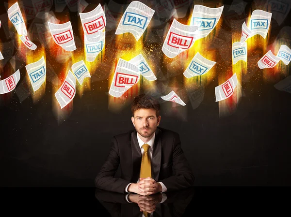 Depressed businessman sitting under burning tax and bill papers