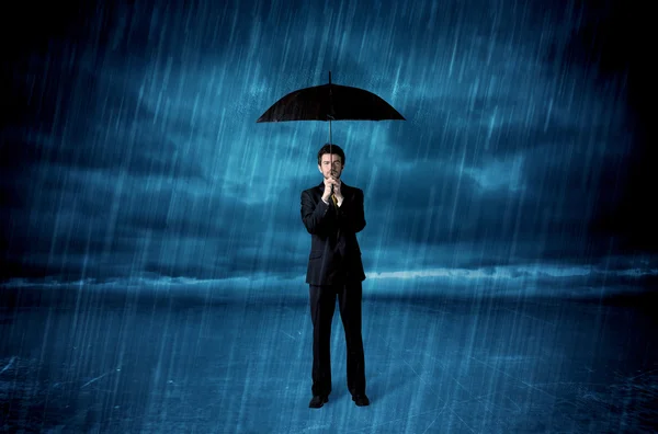 Business man standing in rain with an umbrella