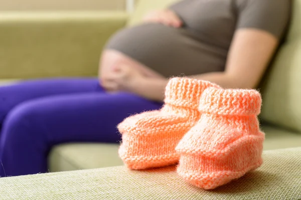 Booties on the couch next to a pregnant woman