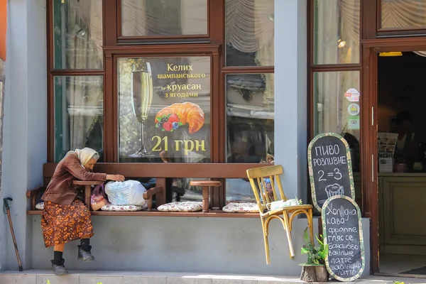Old woman sitting near entrance of restaurant in Lviv, Ukraine