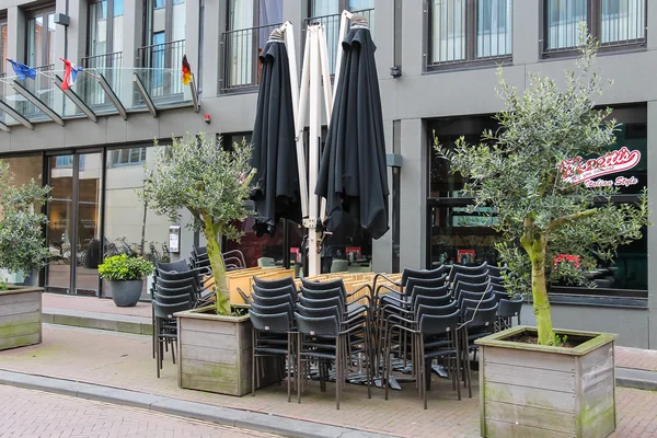 Folded cafe tables and chairs and closed sun umbrellas on the si