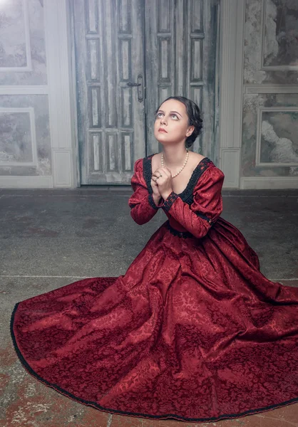 Beautiful medieval woman in red dress praying