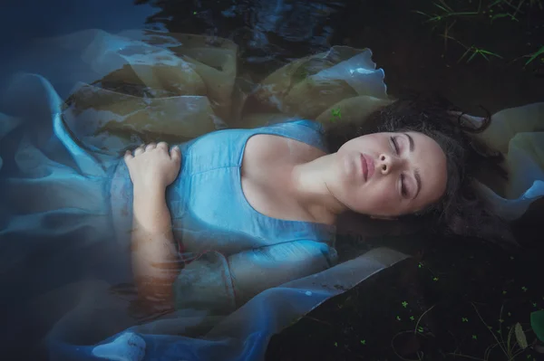 Young beautiful drowned woman in blue dress lying in the river