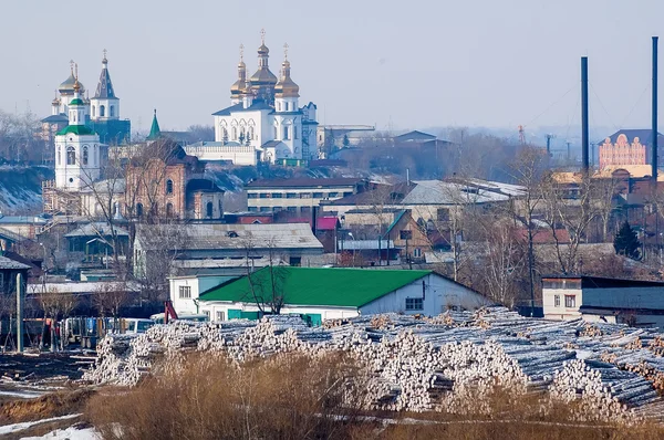 Big pile of logs and two churches. Tyumen. Russia