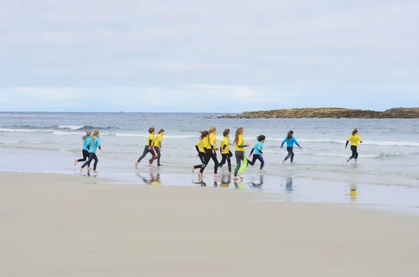 Group of young children running out to sea for surfing lesson